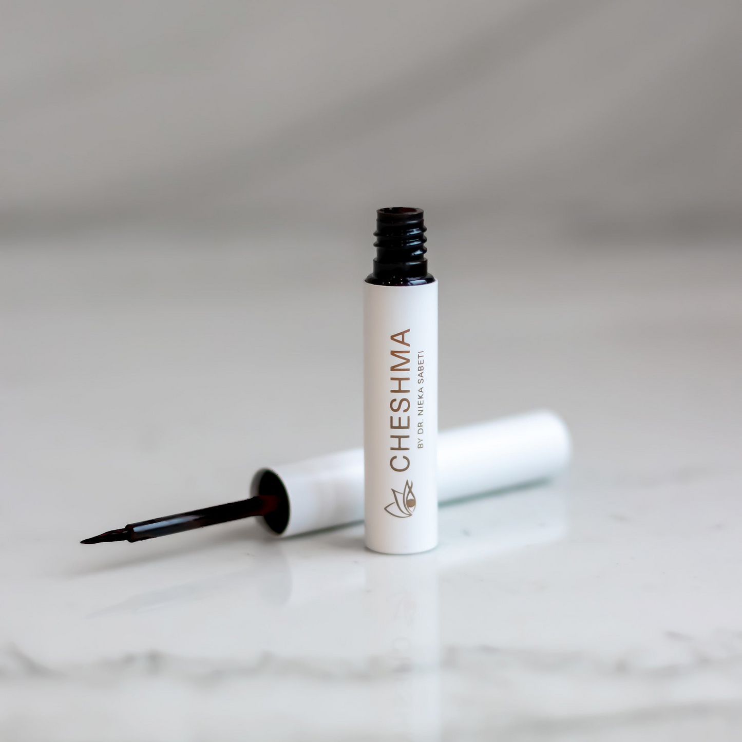 Luxury black liquid eyeliner on white vial on marble counter.