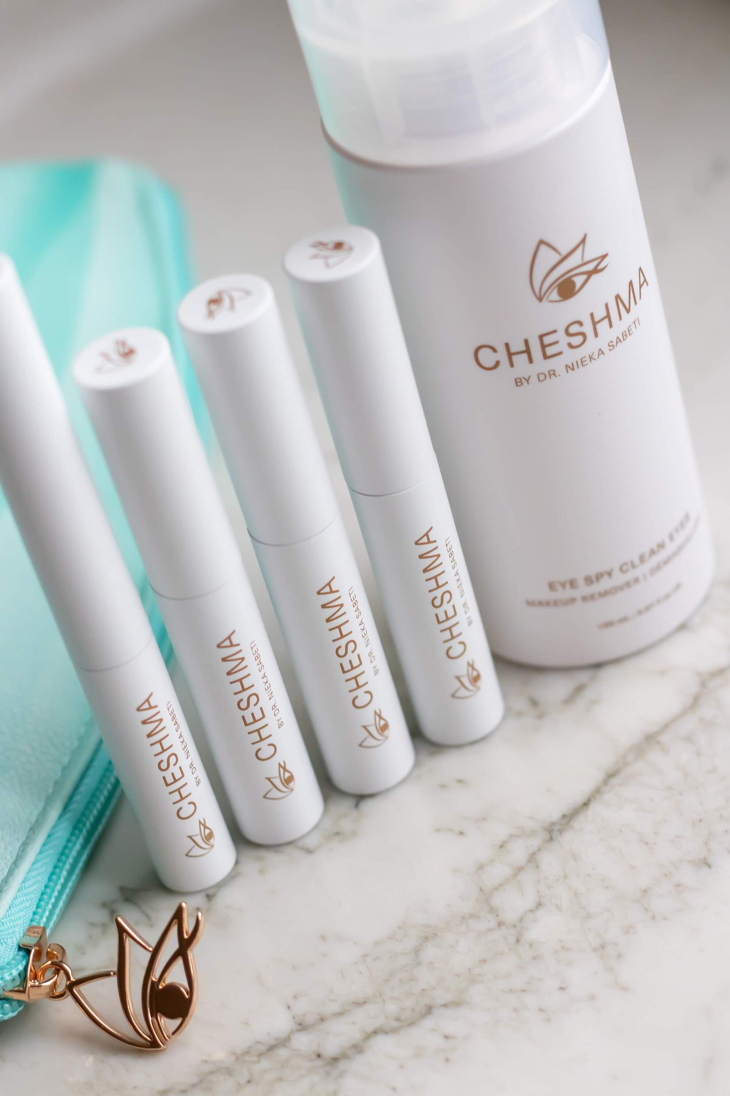 Cheshma products in white containers on marble counter with blue bag and gold eye logo zipper