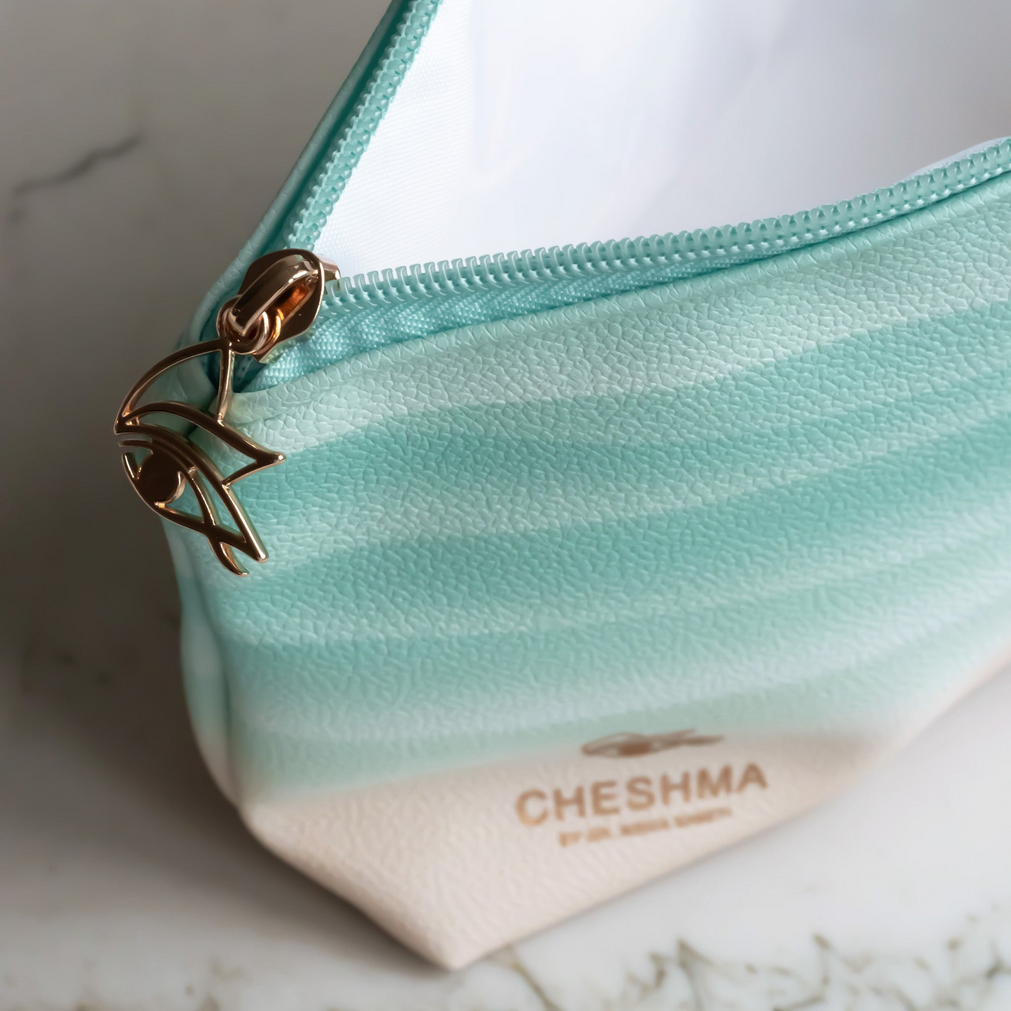 Teal waved pouch with gold zipper on a marble surface, featuring the brand 'Cheshma'.