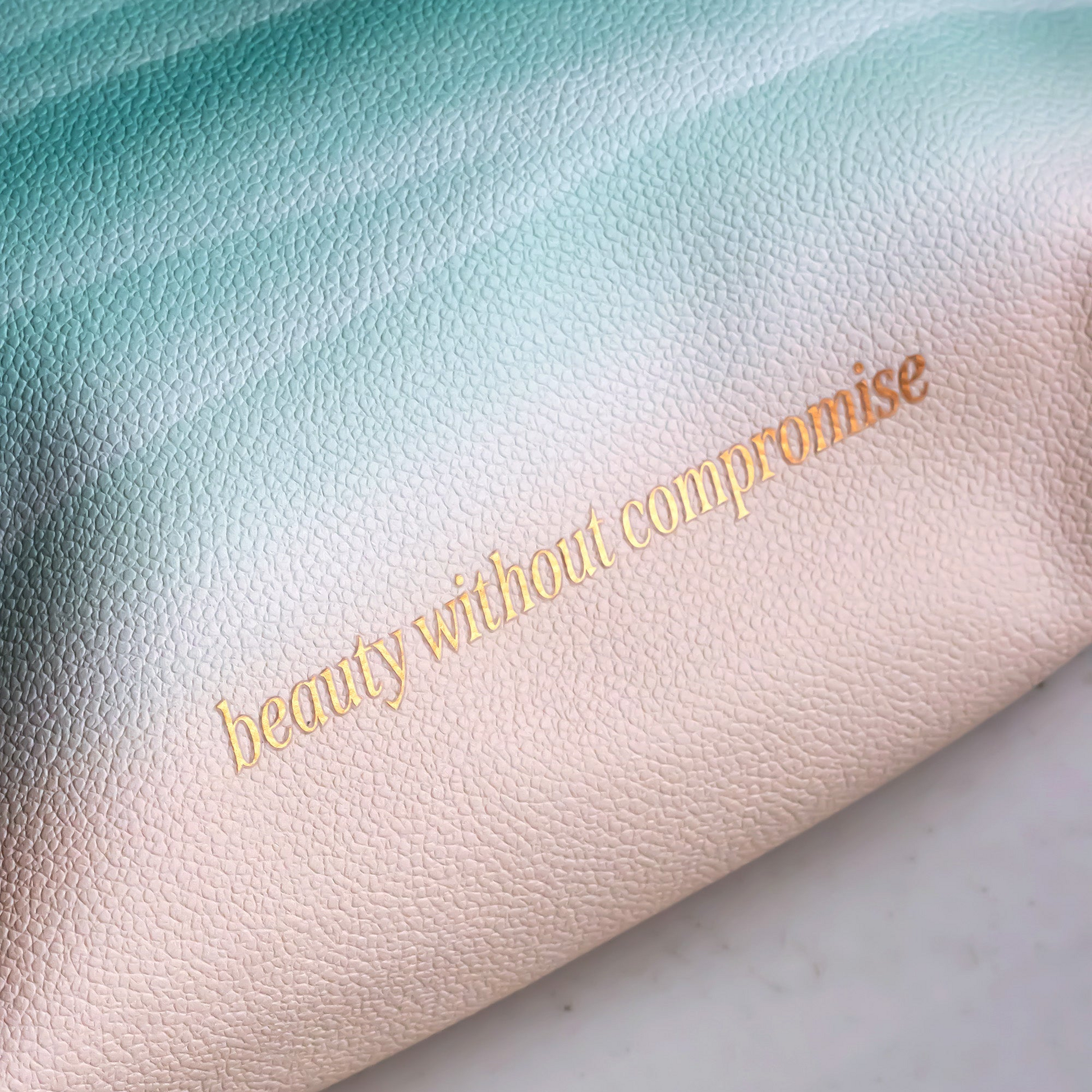 Gradient pouch with 'beauty without compromise' text on a marble surface
