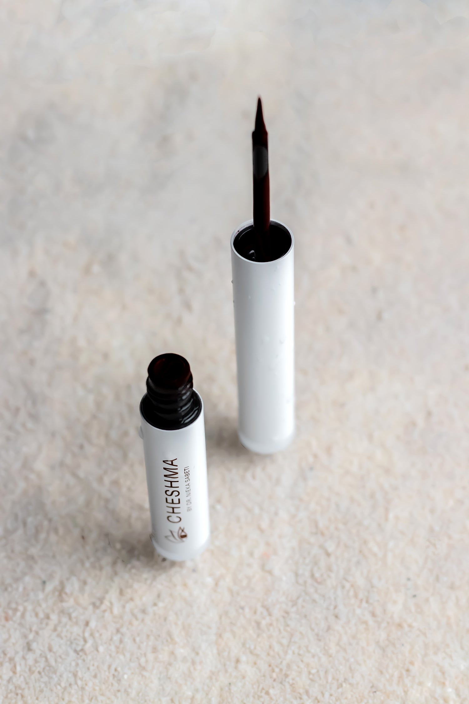 Two bottles of Cheshua eyeliner on a textured beige surface