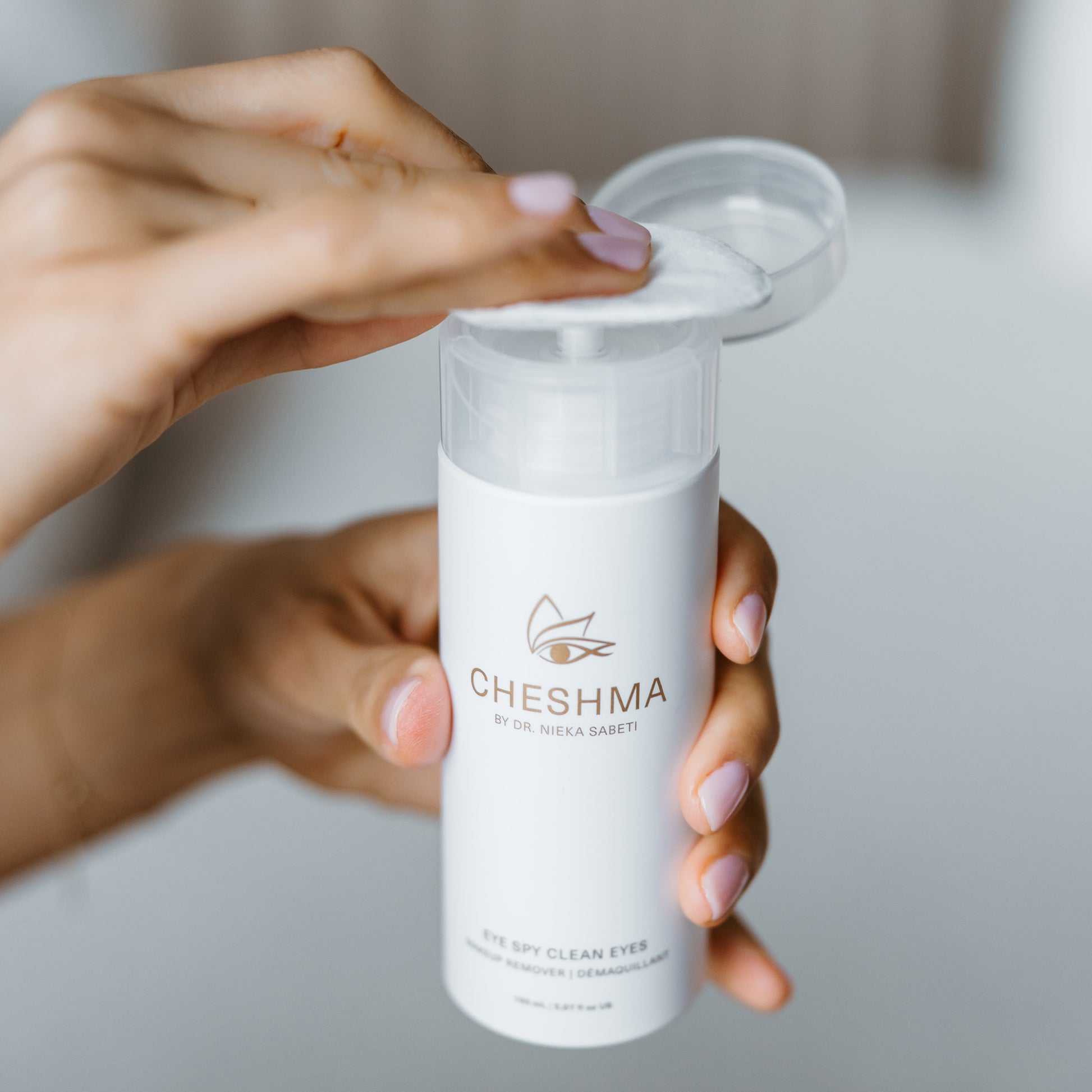 A woman holds a bottle of Cheshma eye makeup remover, showcasing its elegant design and clean packaging.